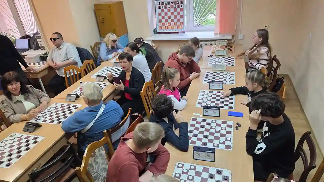 взрослые и дети —  участники инклюзивного шашечного турнира между незрячими и неслышащими во время игры 